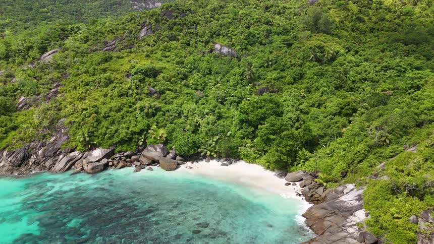 An aerial shot reveals a stunning secluded cove with crystalclear turquoise waters and a small white sand beach the cove is framed by lush green rocky cliffs and large boulders highlighting its pristine and untouched nature