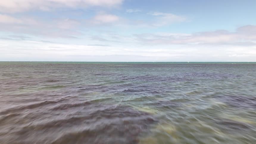 Smooth jagged rocks jut out of shallow clear water along a calm shoreline under a partly cloudy sky