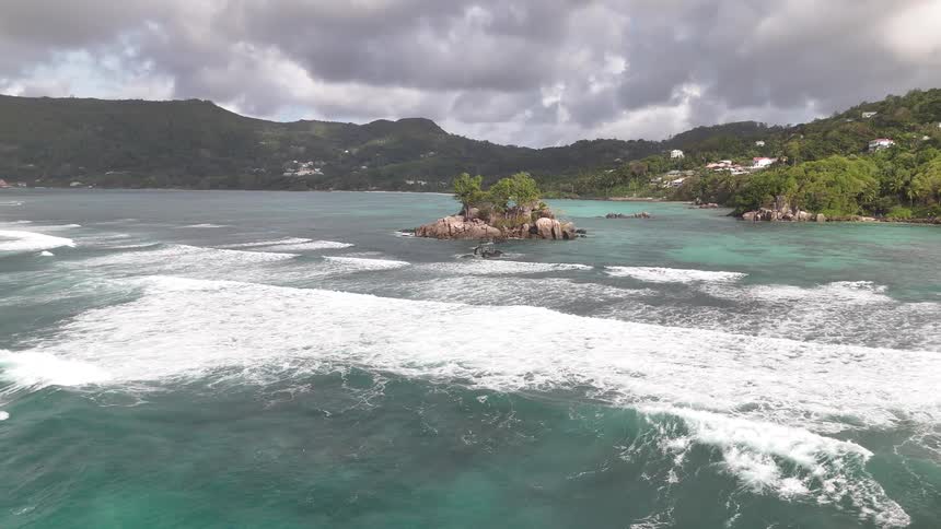 A small island in the ocean is located near a mountainous shore covered in forest and vegetation