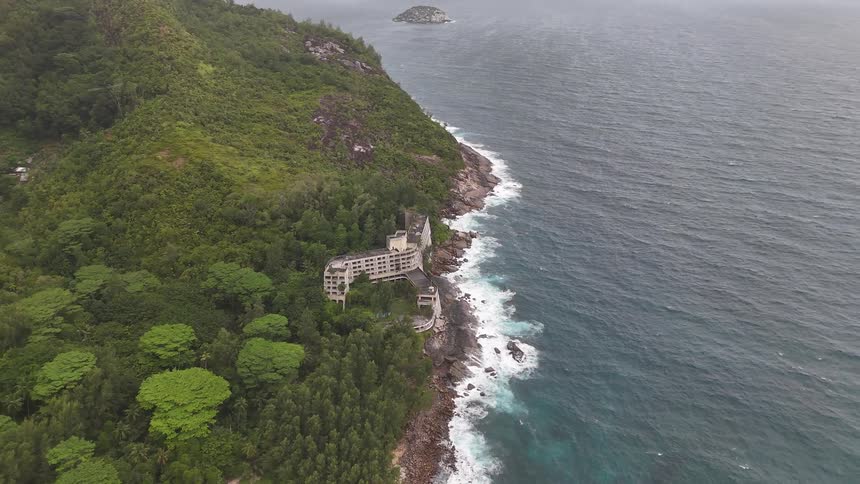 Aerial of secluded waterfront hotel nestled in hillside along rocky shoreline on an island