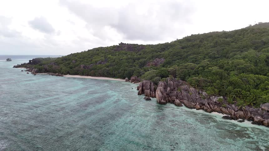 A mountainous island surrounded by rocks as ocean waves hit the shore