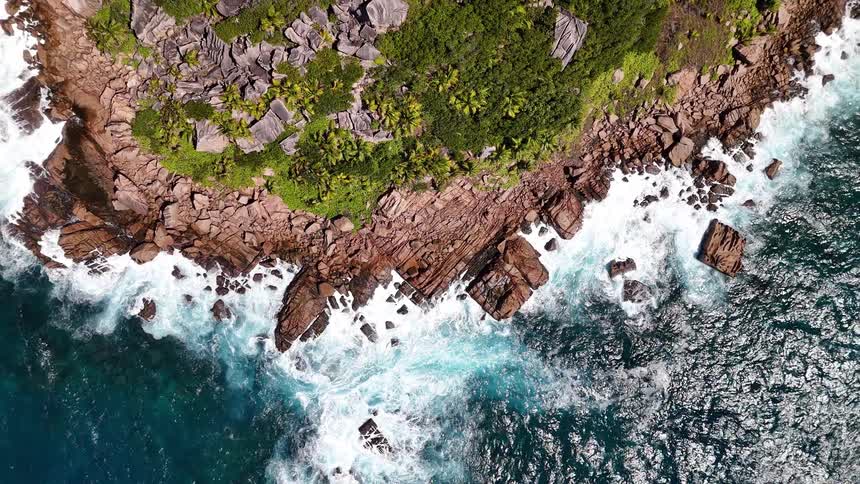 Waves crash against a rugged rocky coastline covered in dense green vegetation