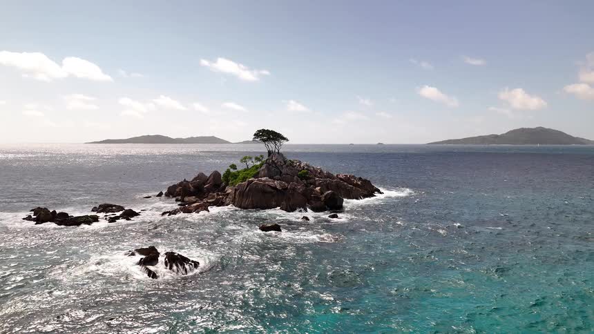 A tiny rocky islet with a few windswept trees rises from choppy blue waters framed by distant islands