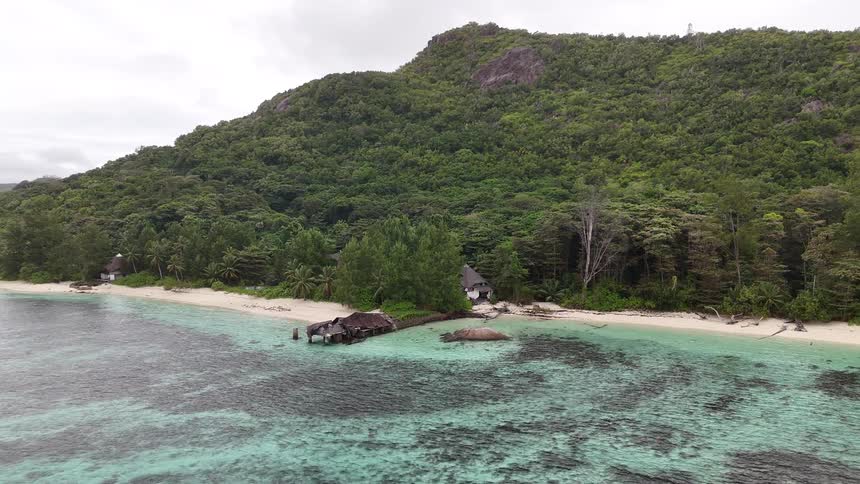 Aerial view of a tropical beach lined with dense forest and clear turquoise water