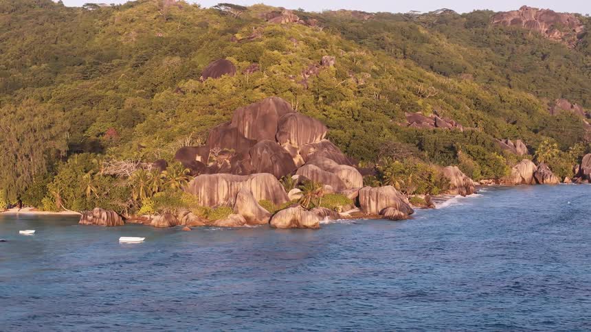 A rocky island with boats floating near the shoreline at midday