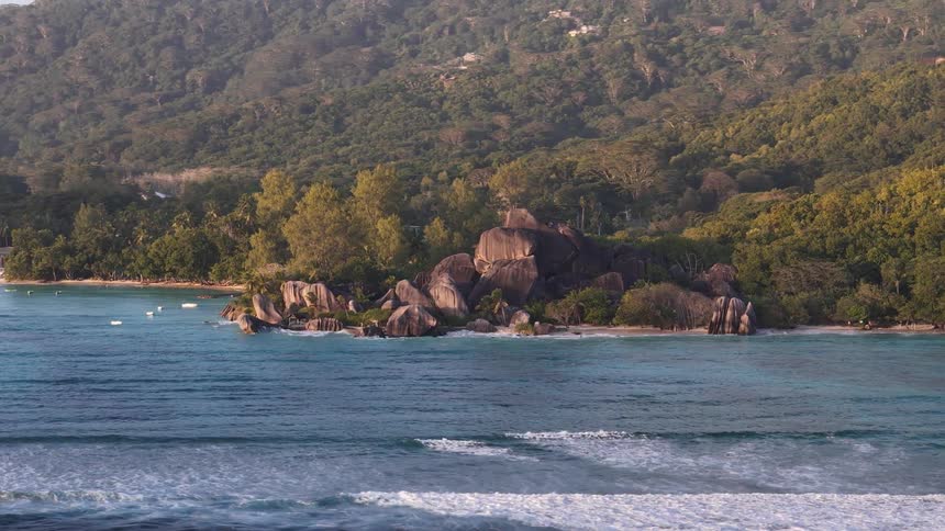 A forested island with ocean waves hitting the shore at midday