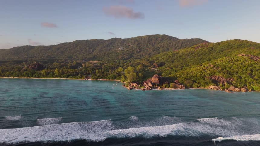 A mountainous island surrounded by rocks as ocean waves hit the shore