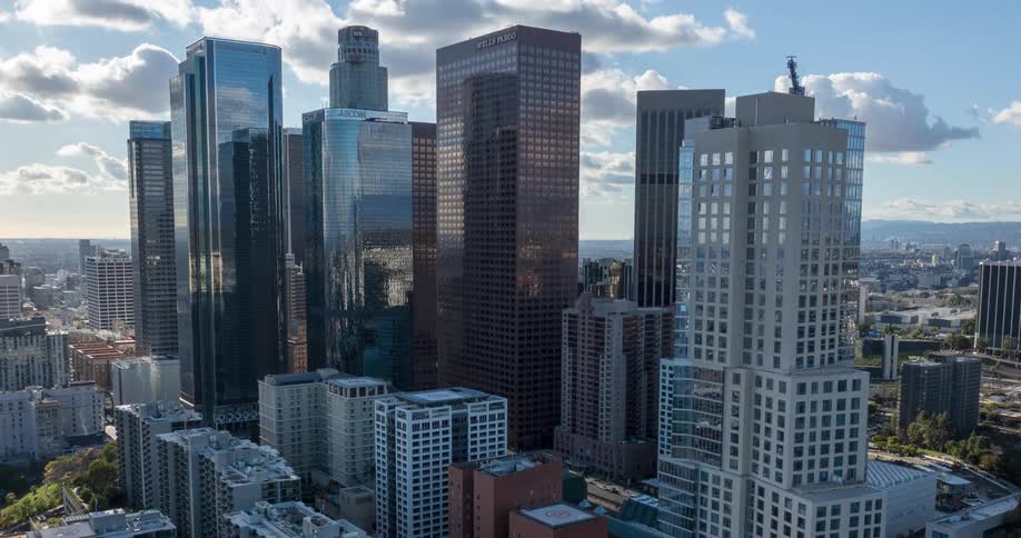 A city skyline with tall glass and brick buildings rises under a partly cloudy sky