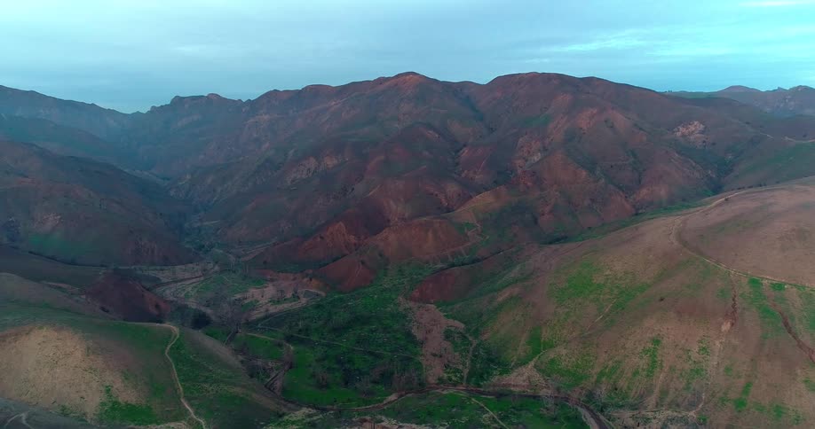 Rolling hills and rugged mountains in Malibu stretch across the horizon marked by dirt paths and sparse vegetation