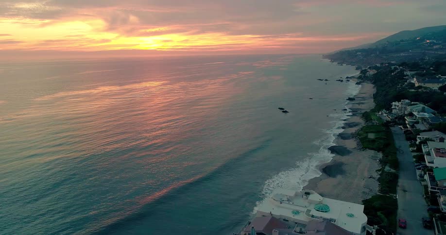 Aerial view of houses on the beachfront with a reddish sunrise sky in Malibu