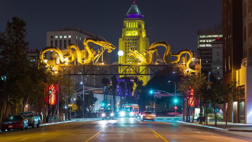 A pair of illuminated golden dragon sculptures span a street in downtown Los Angeles Chinatown  with city hall glowing in the background