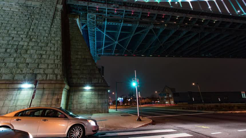 A busy street intersection under a bridge in a city at night