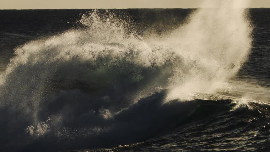 Waves are crashing in the ocean at sunset