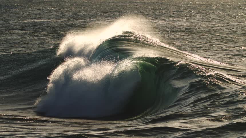 A large ocean wave is cresting with white foam at the top creating a dramatic and powerful scene