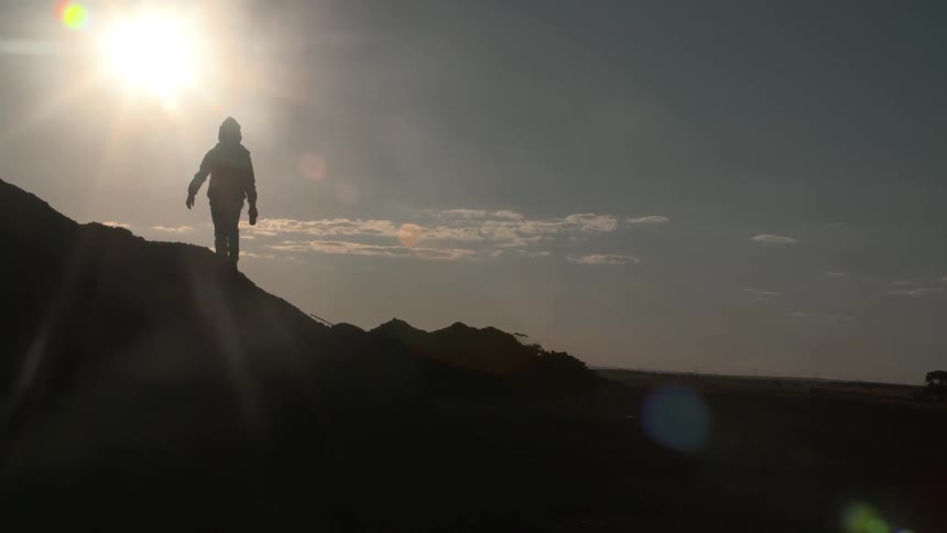 Silhouette of a person on a hill with the sun shining down