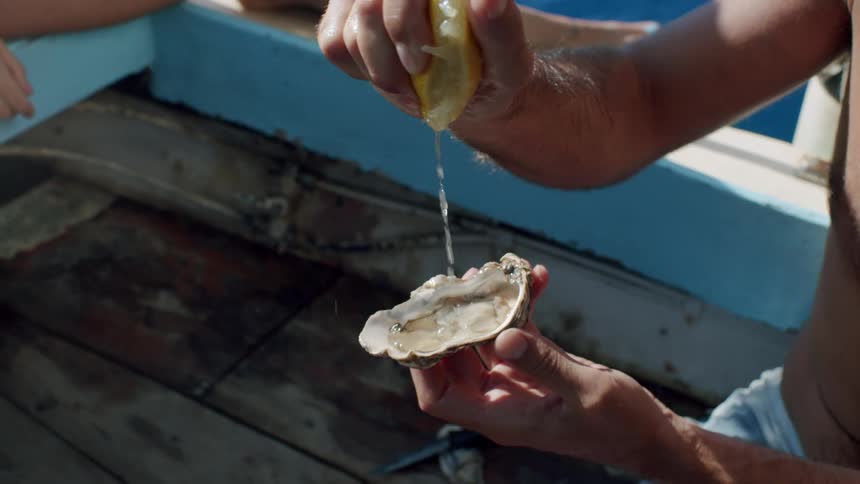A person squeezes lemon juice onto a freshly opened oyster while seated on a boat