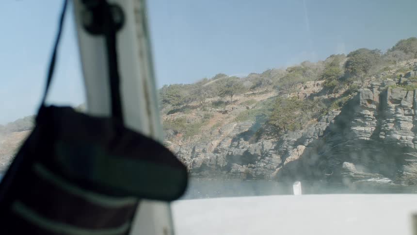 Woman wearing a swimsuit dives off a boat floating near a coastal cliff on a summer day