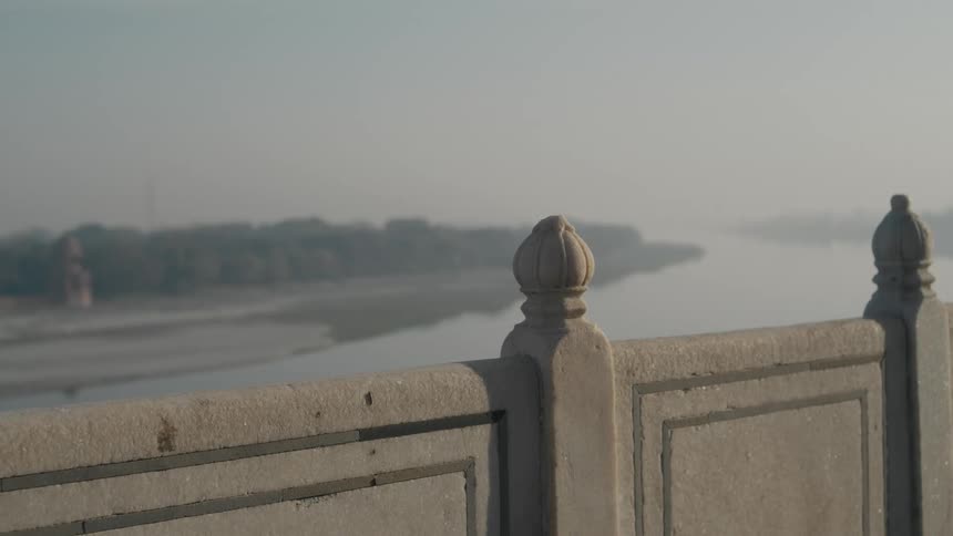 A hazy riverfront scene viewed from behind a stone railing at dawn or dusk