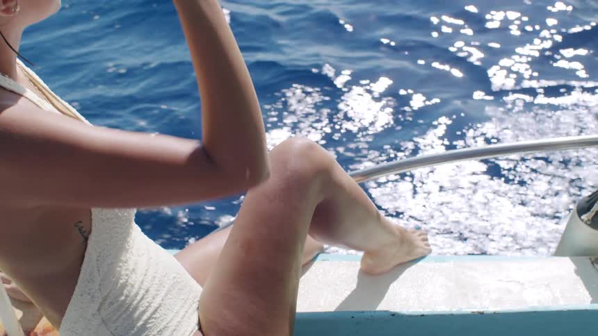 Woman in white swimsuit sitting on a yacht moving through the sea