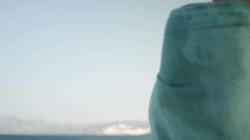 A person stands near the ocean gazing at the distant coastal town across the water