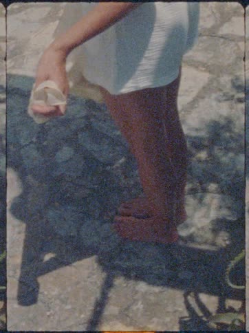 A person stands barefoot on sunlit stone holding a light fabric in one hand