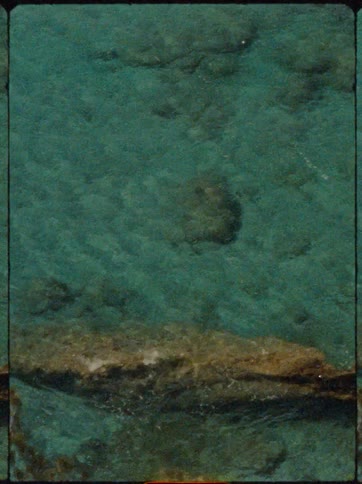 Sunlight reveals the texture of rocks beneath the surface of clear turquoise water
