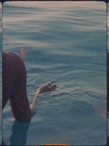 A persons arm drifts gently in rippling blue water catching the soft light