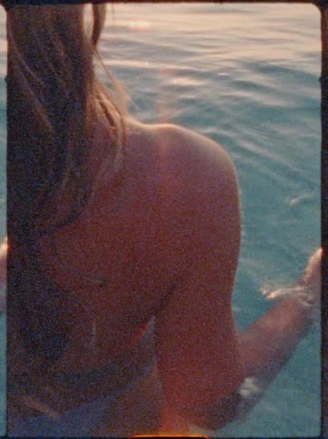 A woman relaxes in the water facing a serene sunset over the sea