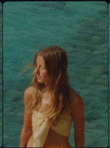 A woman with long blonde hair basks in the sunlight near vibrant blue water