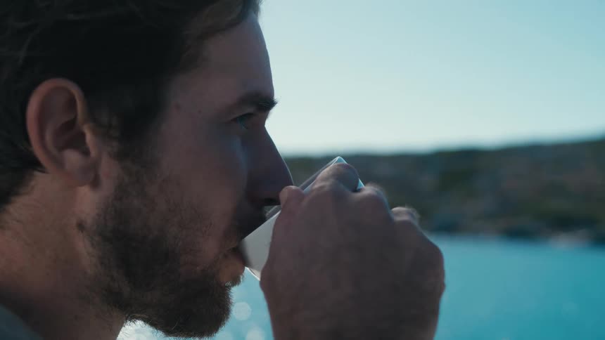 Man drinking from a white cup in a seaside setting