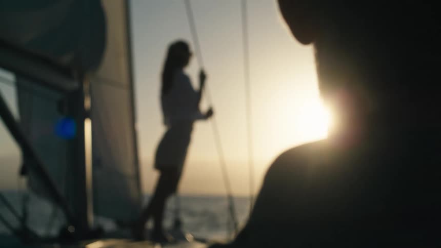 Sun shining from a red sky casts the two people on a sailboat into silhouette