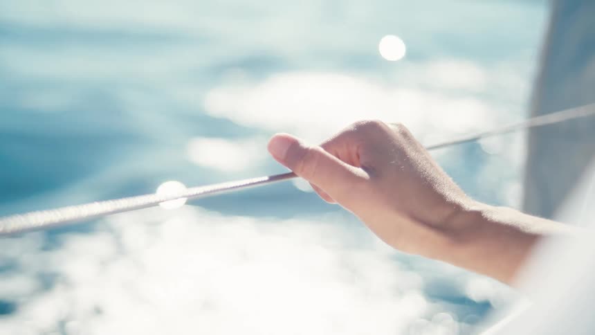 A persons hand grips a rope on a boat with the sparkling ocean blurred in the background