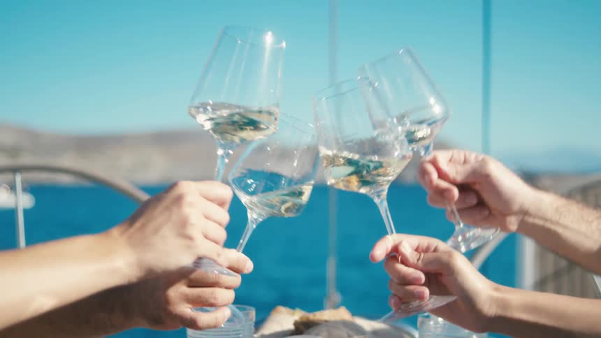 Four people toasting glasses of white wine in a seaside setting