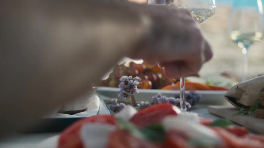 A hand reaches over a colorful spread of tomatoes herbs and wine on a shared table