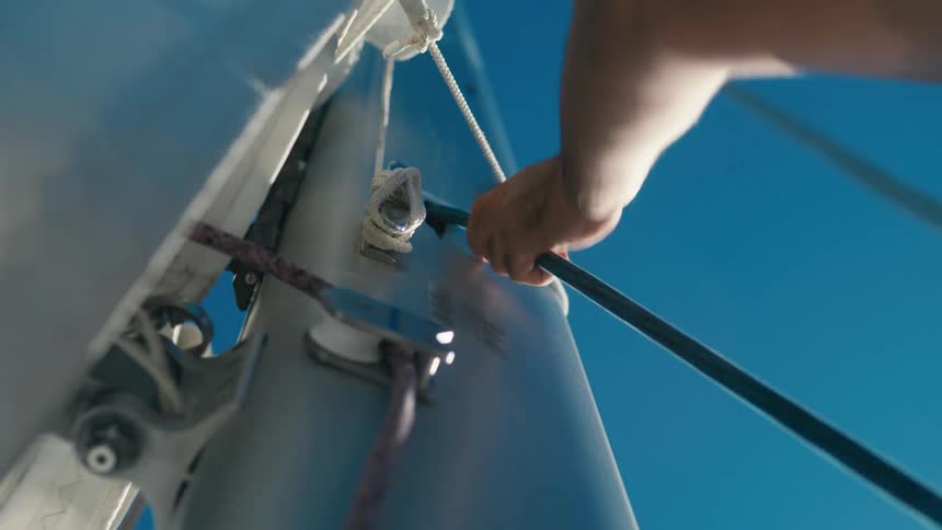 A hand pulls a rope taut on a sailboat under a bright blue sky