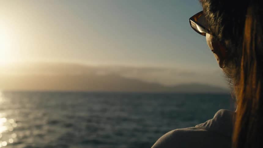 Woman with glasses by the sea at sunset