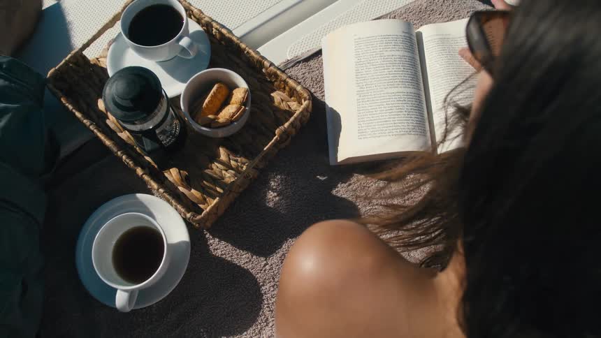 Woman sitting reading a book next to a box with cookies and coffee