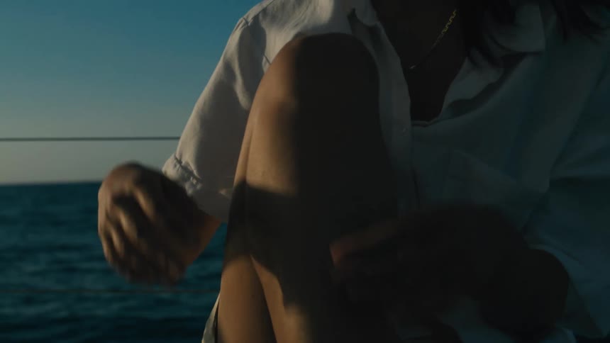 Woman sits curled up on a boat arms wrapped around her knees with the ocean in the background