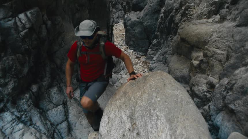 A person navigating a rocky narrow gorge with trees and leaves visible at the top the scene captures the challenging terrain of a canyon or similar natural formation
