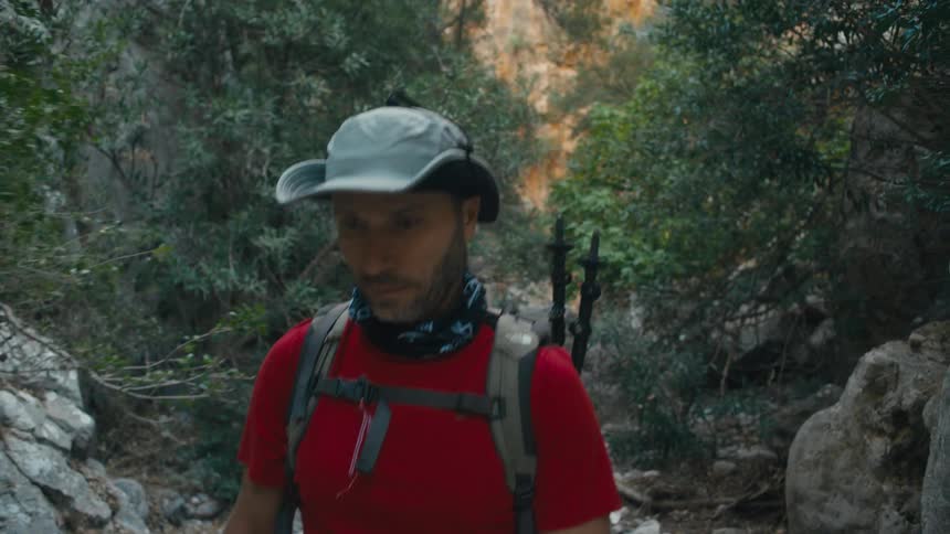 Man wearing a hat walking along a wooded and rocky trail