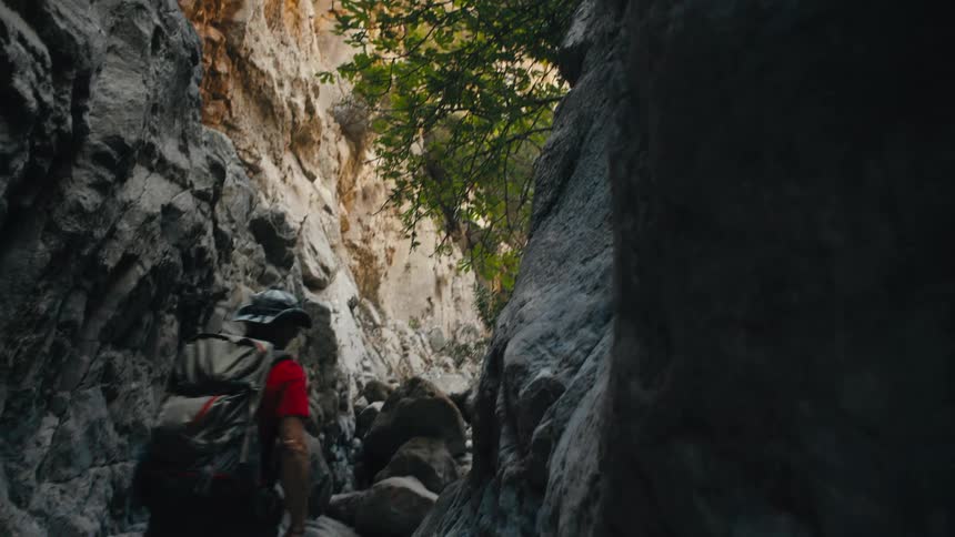 A closeup shot focuses on a persons hand with fingers splayed gently touching the rough textured surface of a large rock or cliff face the background is blurred showing a rocky yellowish cliffside suggesting an outdoor