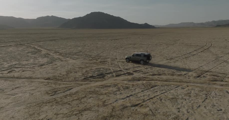 Sports utility vehicle driving across the arid terrain bordering the mountains crosses old vehicle tracks during the daytime
