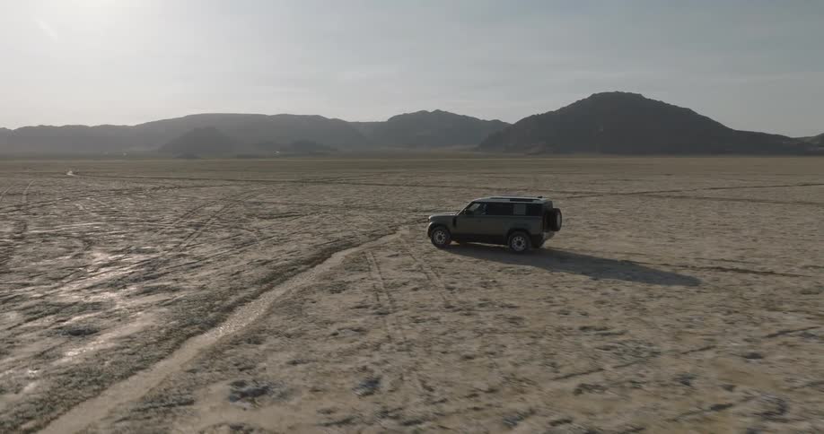 Vehicle traveling in a clay area with mountains on the horizon