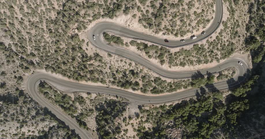 Vehicles drive along a highway snaking through arid scrub land on a summer day