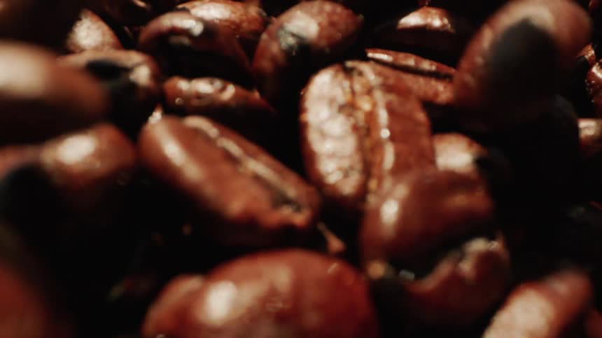 A series of coffee beans is being poured onto the ground outdoors under the sun to dry