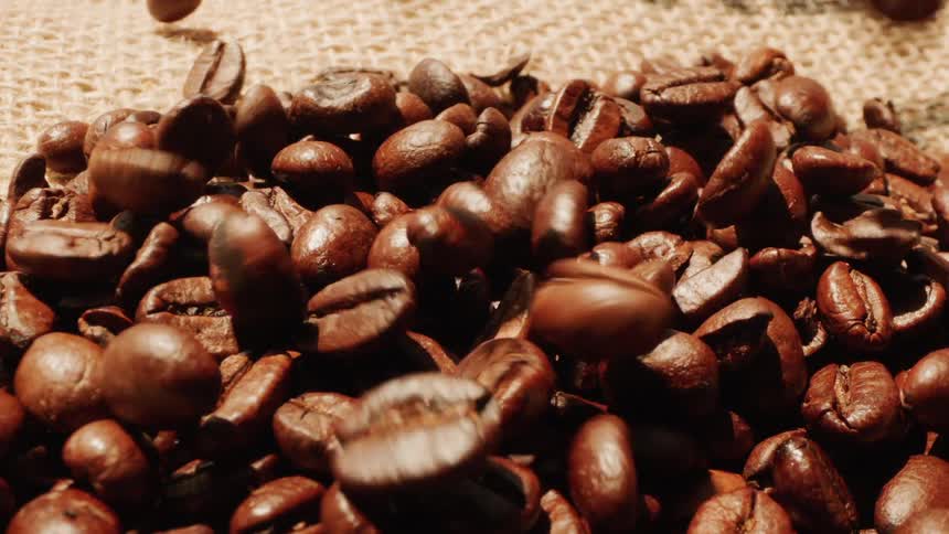 Coffee beans are being poured onto a mat outdoors under the sun to dry