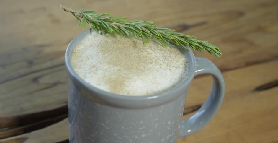 A mug of coffee with a leaf on top is placed on a wooden table