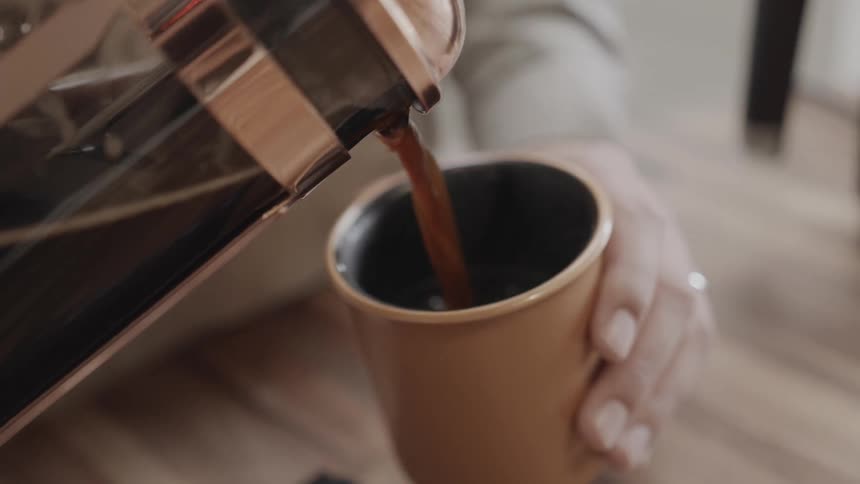 A person is pouring coffee into a mug from a jug