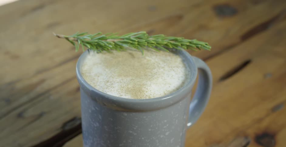 A coffee mug filled with coffee topped with a leaf is placed on a wooden table