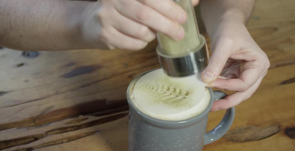 A person is preparing coffee and forming a leaf pattern on top of it
